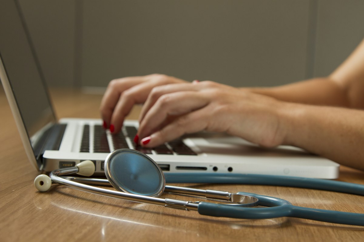 Stethoscope beside a clinician typing visit notes