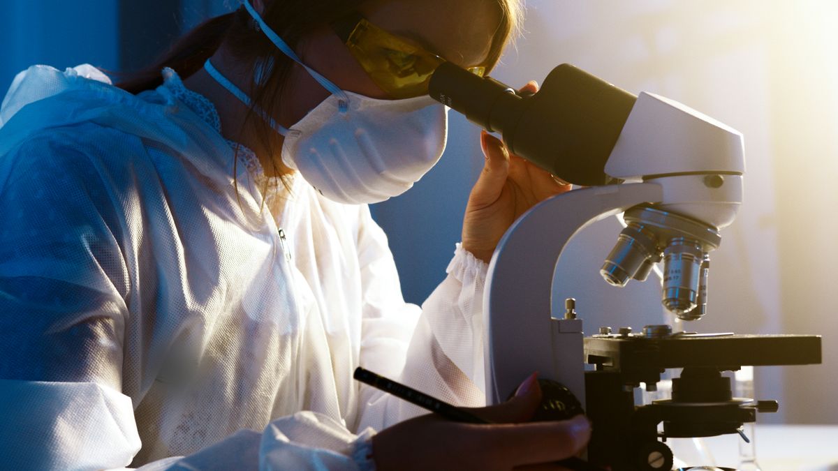 Scientist in a mask looking through a microscope